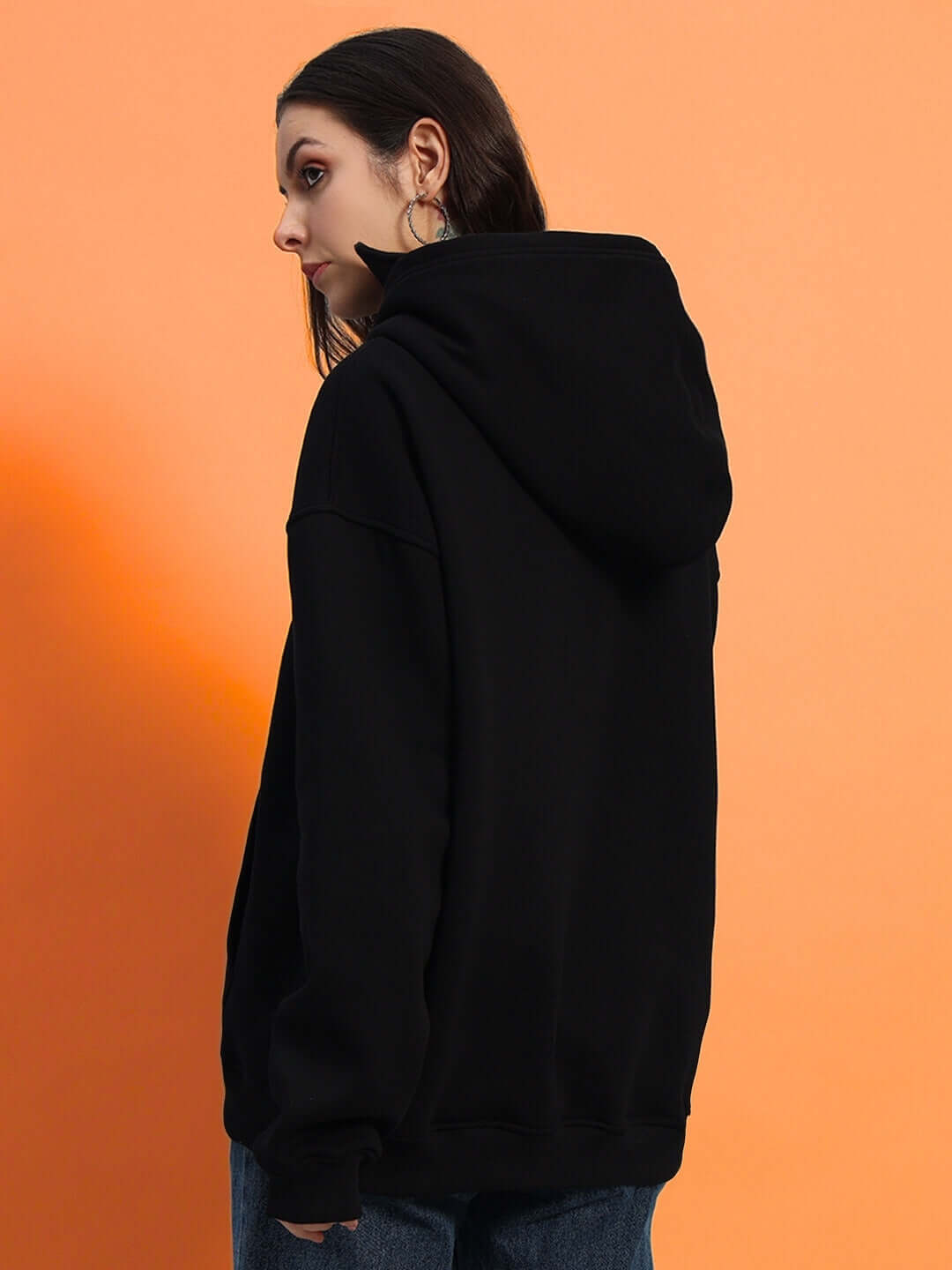 Woman wearing a black oversized fleece hoodie from back view, against an orange background.