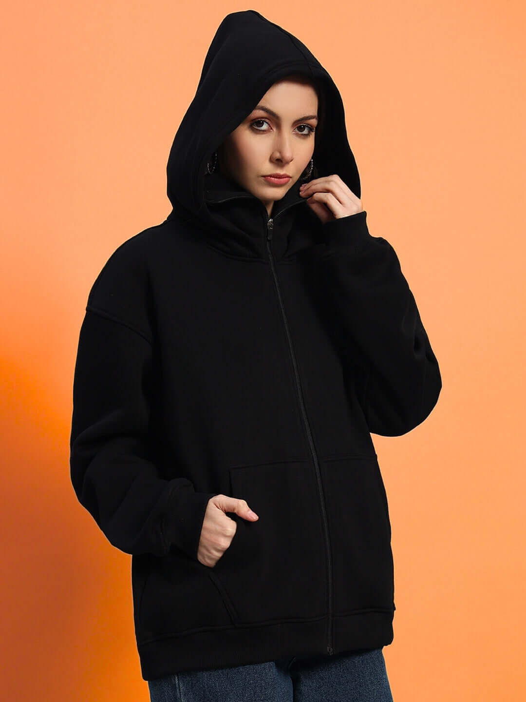 Women's Marksman oversized black fleece hoodie, full front view with hood up against orange background.
