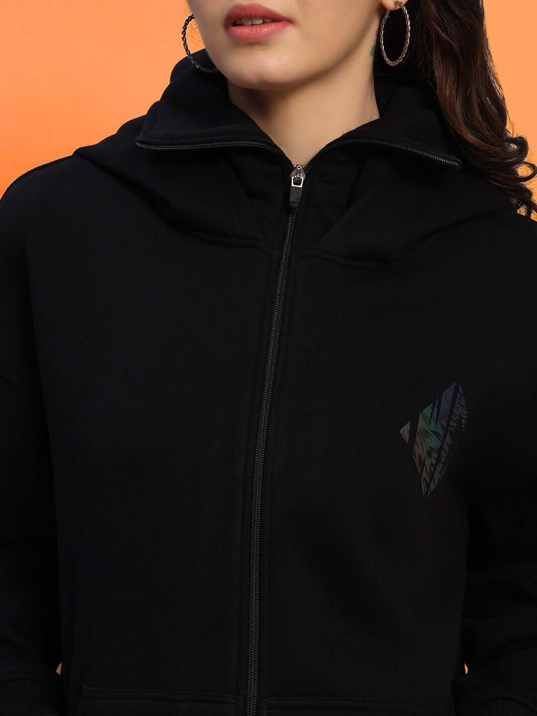 Women's Marksman oversized black fleece hoodie with zipper and logo detail, modeled against an orange background.