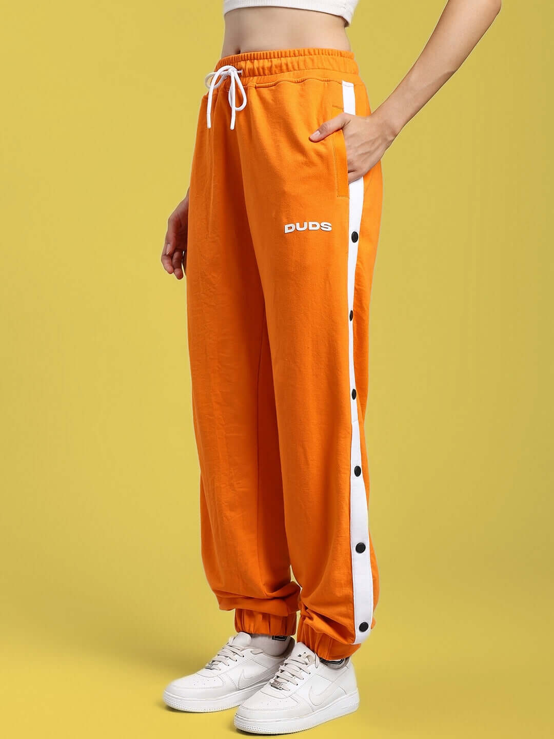 Women wearing WOMENS MILLER RELAXED FIT JOGGERS ORANGE with white side stripes, casual style, yellow background.