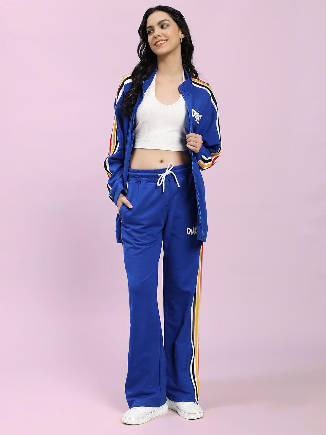 Woman wearing WOMEN MODERN EDGE MULTI-STRIPE JACKET ROYAL BLUE with sporty stripes, paired with matching pants and white top, showing sporty style.