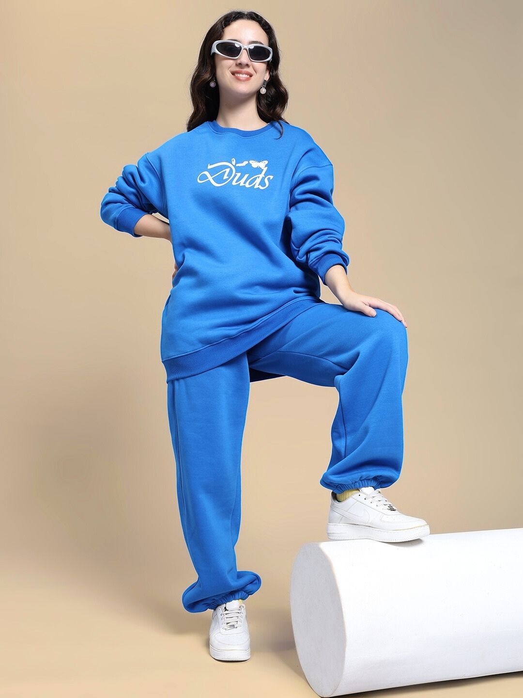 Model wearing WOMEN'S NATURE LINK FLEECE JOGGER ROYAL BLUE outfit, posing confidently in stylish sunglasses and white sneakers.