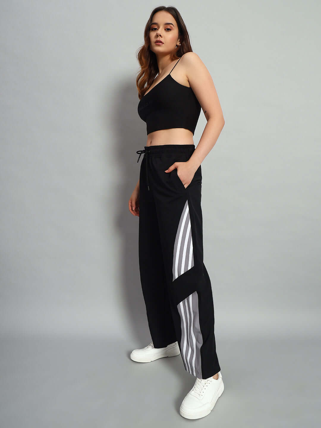 Model wearing women's black cargo pants with relaxed fit and stripe detail, paired with a black top and white sneakers.
