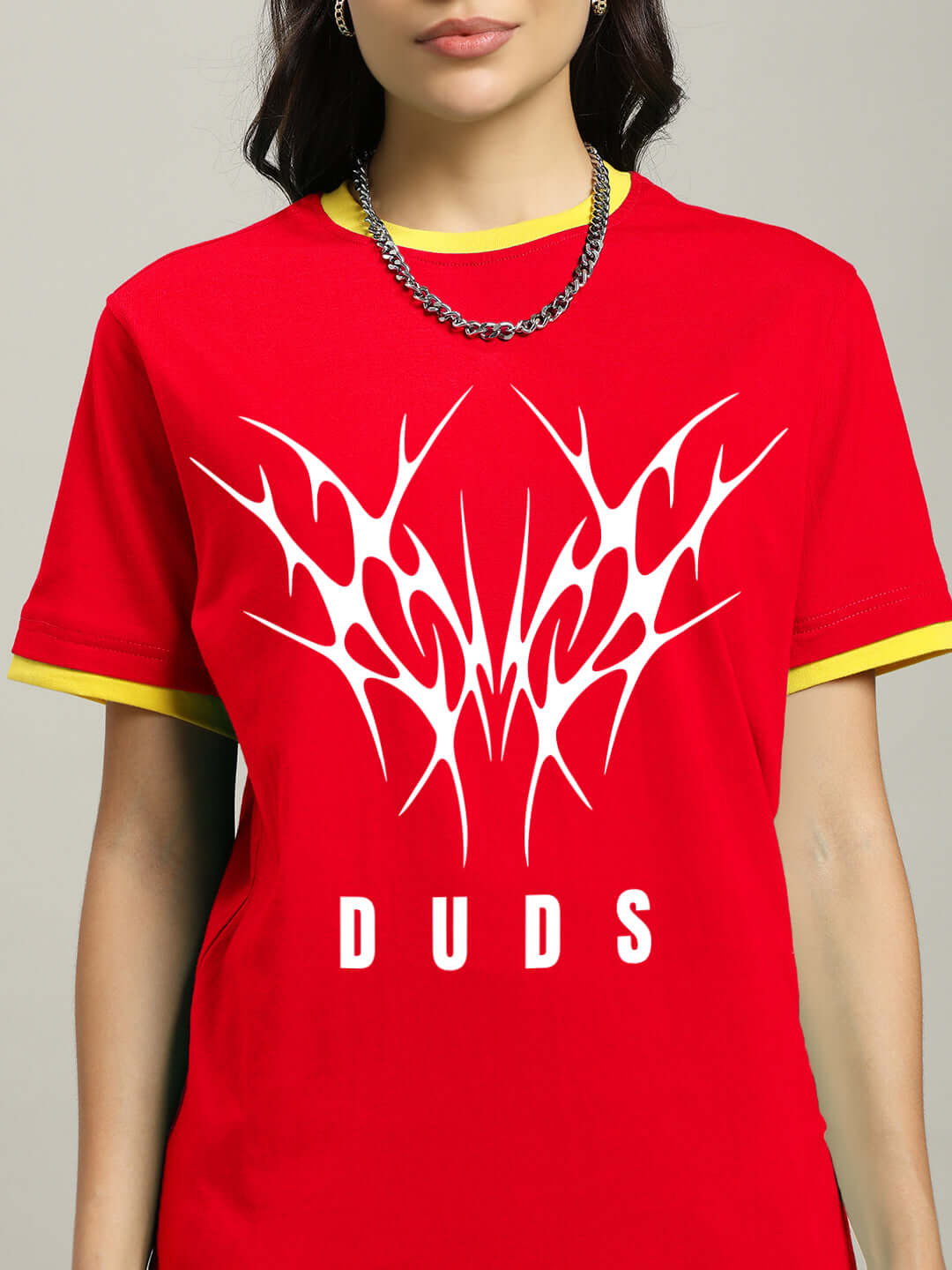 Woman wearing a red regular fit T-shirt with graphic design and text 'DUDS,' featuring yellow accents and a chain necklace.