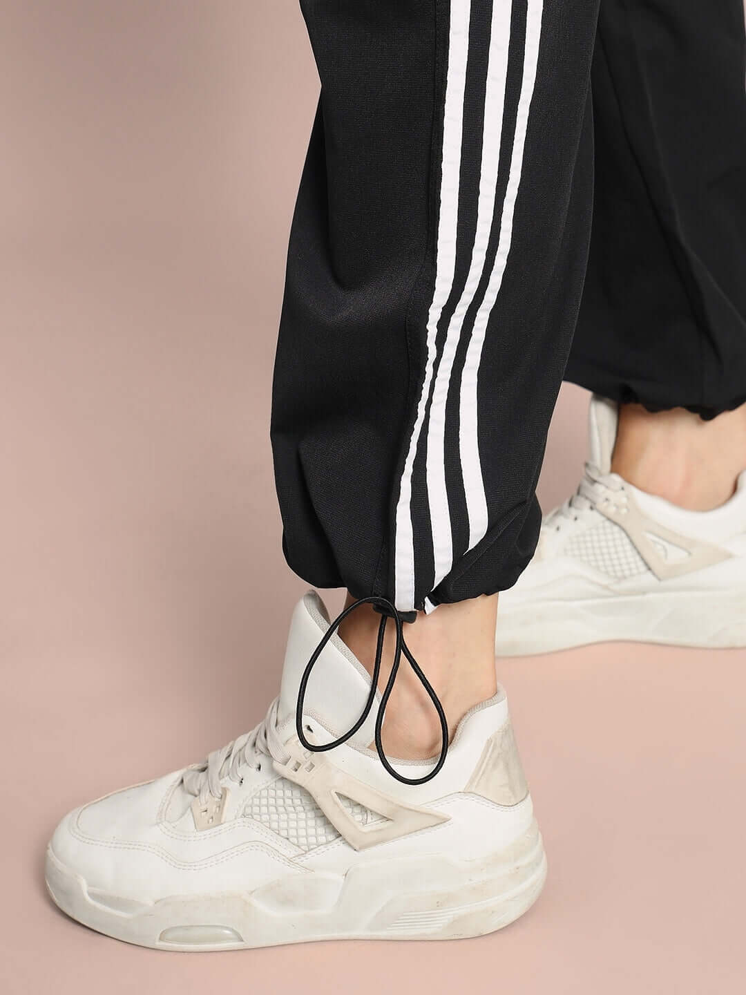 Close-up of black relaxed fit cargo pants with white stripes and adjustable drawstring ankles, styled with white sneakers.
