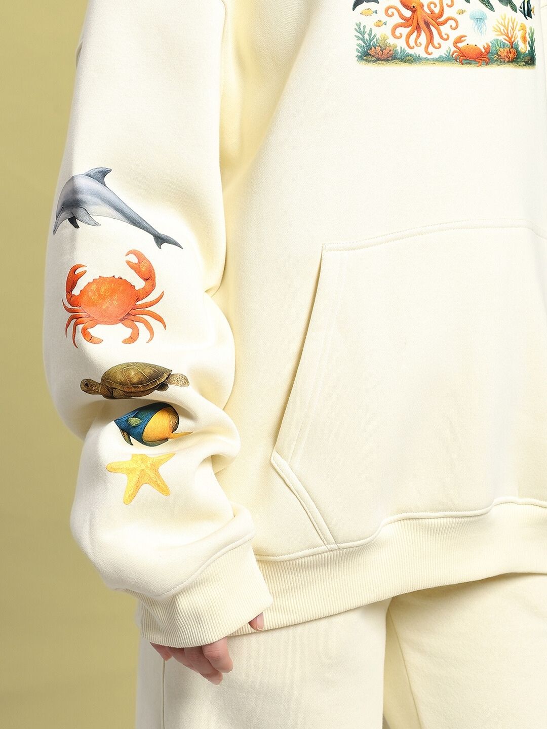Close-up of sleeve design on WOMEN'S OCEAN BUDDIES OVERSIZED FLEECE HOODIE OFF-WHITE with marine animal illustrations.