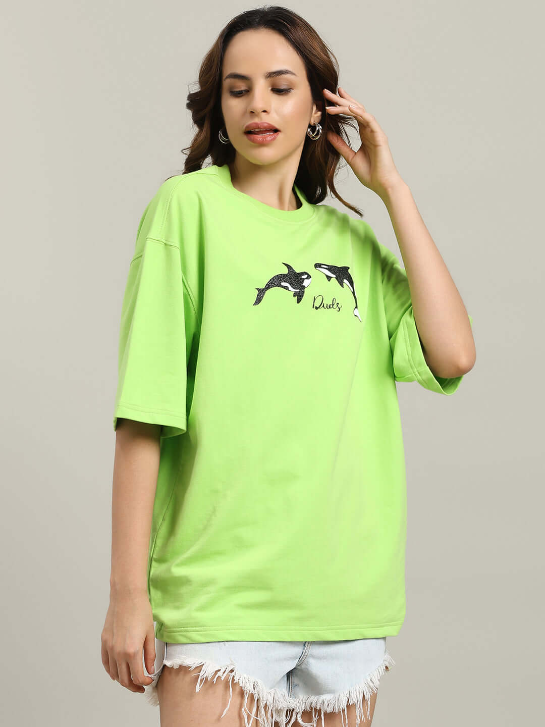 Model wearing WOMEN'S ORCAS OVER-SIZED T-SHIRT NEON GREEN with orca graphics, highlighting bold streetwear style.