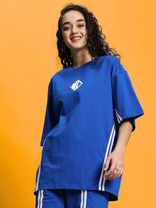 Model wearing women's oversized blue T-shirt made of premium cotton fabric. Features stylish design with white stripes and is bio-washed.