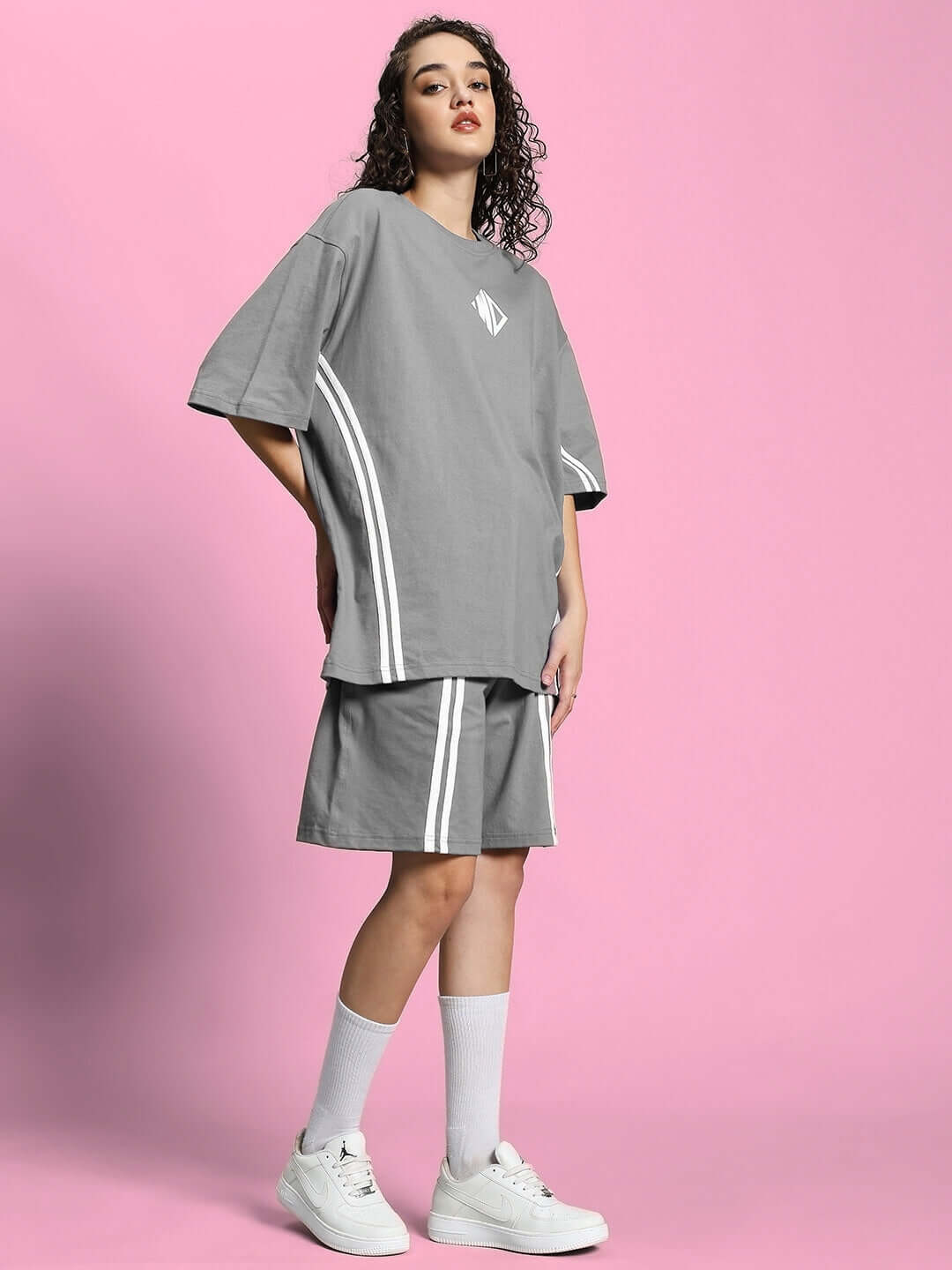 Woman wearing WOMEN'S OUTLOOK SUMMER CO-ORD SHORTS SET GREY with relaxed-fit t-shirt and shorts, on pink background.