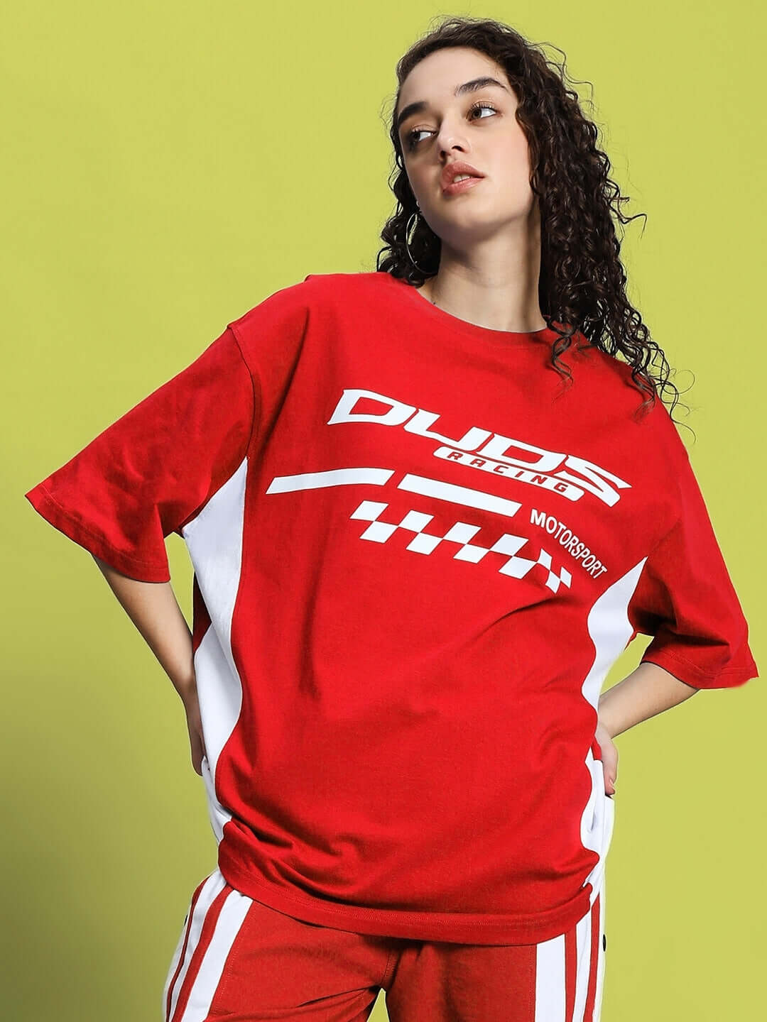 Woman wearing an oversized red Indy Classic T-shirt with white graphic print, made from premium cotton blend, against a lime green background.