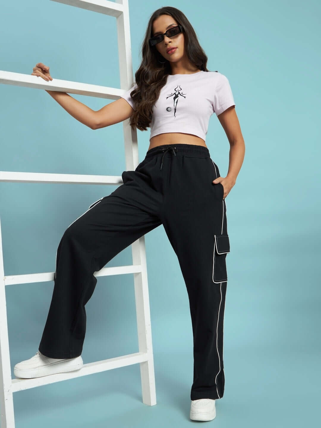 Model wearing black women's pedal contrast stitch cargo pants with white sneakers and a crop top, standing against a ladder.