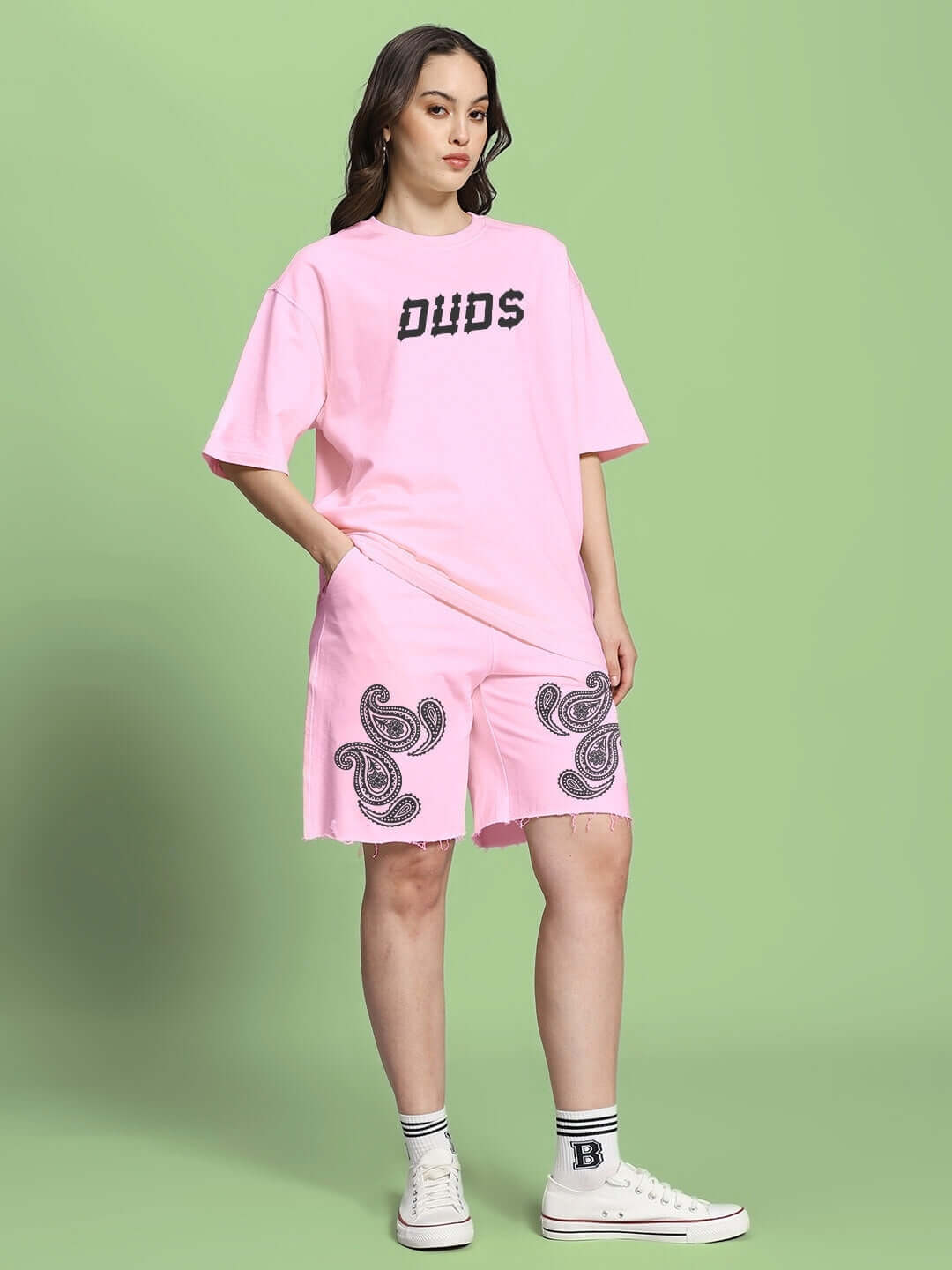 Model wearing WOMEN'S MESSI PAISLEY PRINT CO-ORD SET PINK with paisley design, featuring t-shirt and shorts against green background.