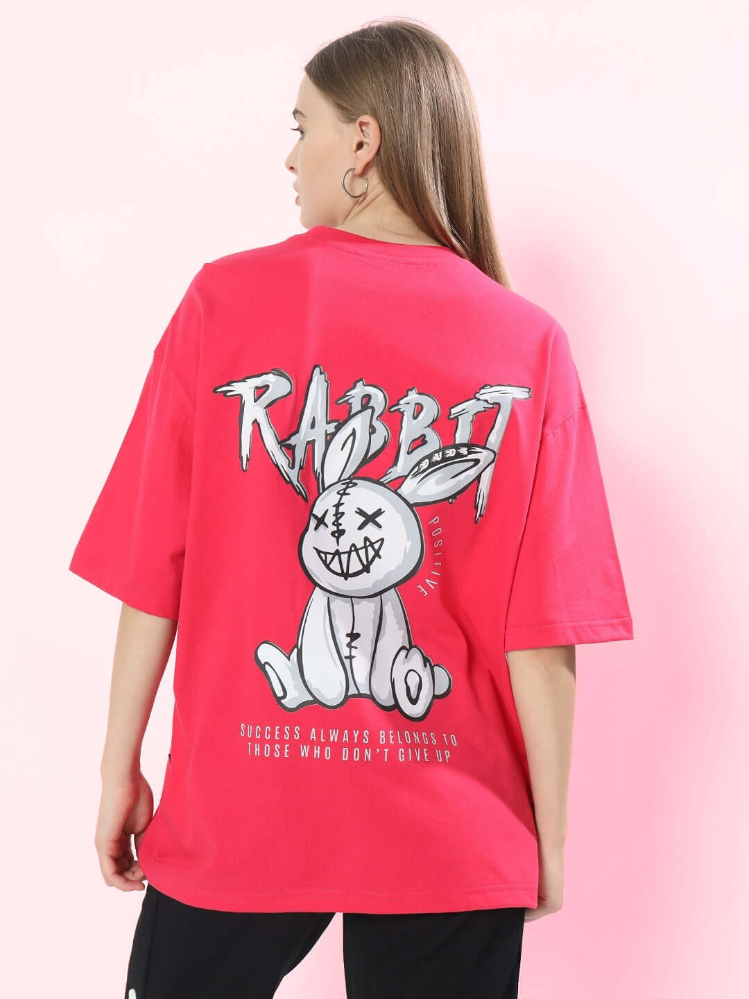 Woman wearing a pink oversized T-shirt featuring a graphic rabbit design with motivational quote, made of 100% cotton.