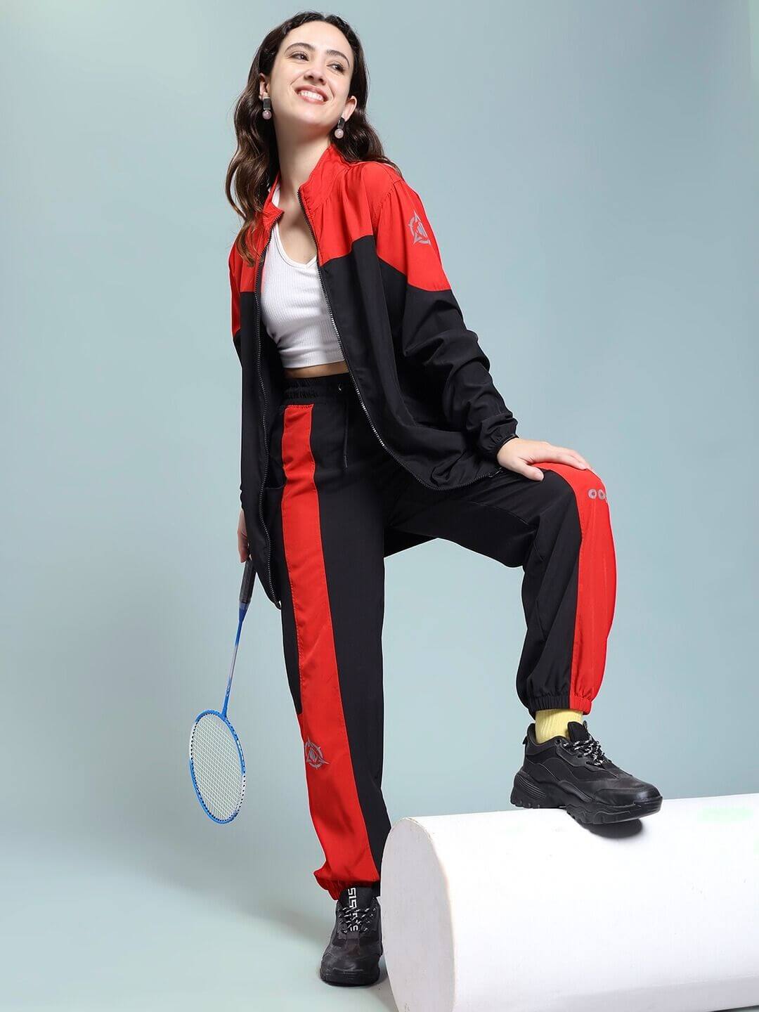 Woman wearing WOMEN POWER BLOCK RELAXED FIT JACKET BLACK RED holding a badminton racket, showcasing sporty and stylish design.
