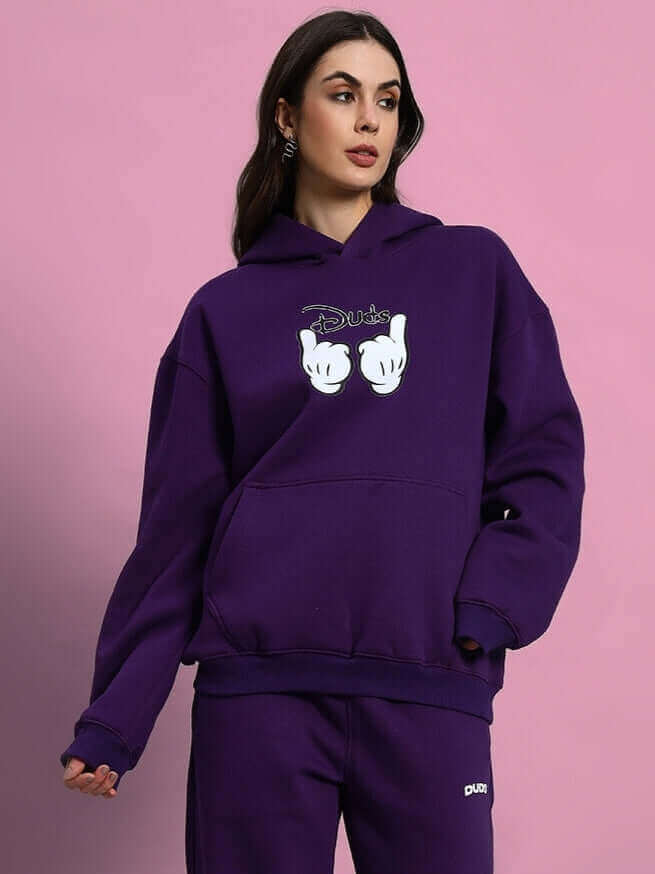 Model wearing WOMEN SUPREME FLEECE HOODIE PURPLE against a pink background, showcasing its plush texture and chic design.
