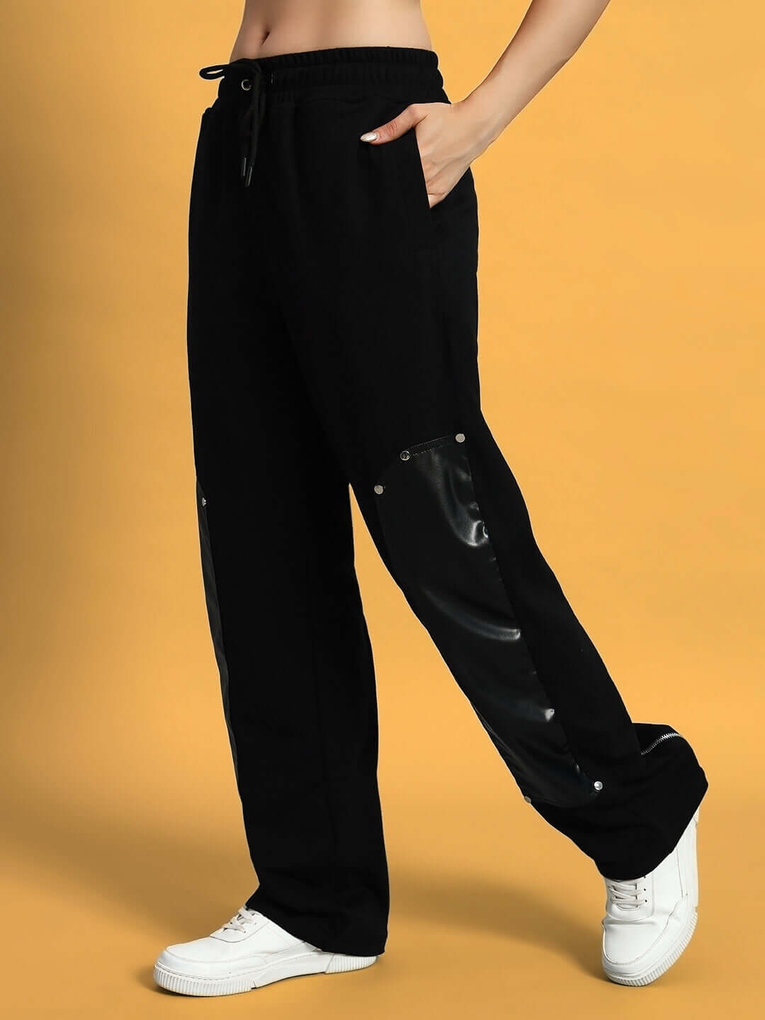 Black women's joggers with raccoon leather patches, showcased in a side pose against a yellow background.