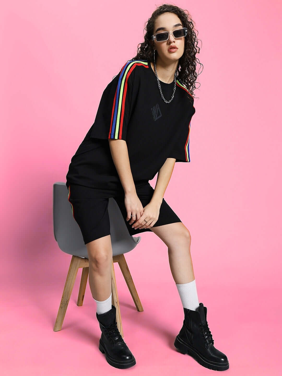 Model wearing WOMEN'S RAINBOW SUMMER CO-ORD SET BLACK with colorful stripes, casual pose against pink background.