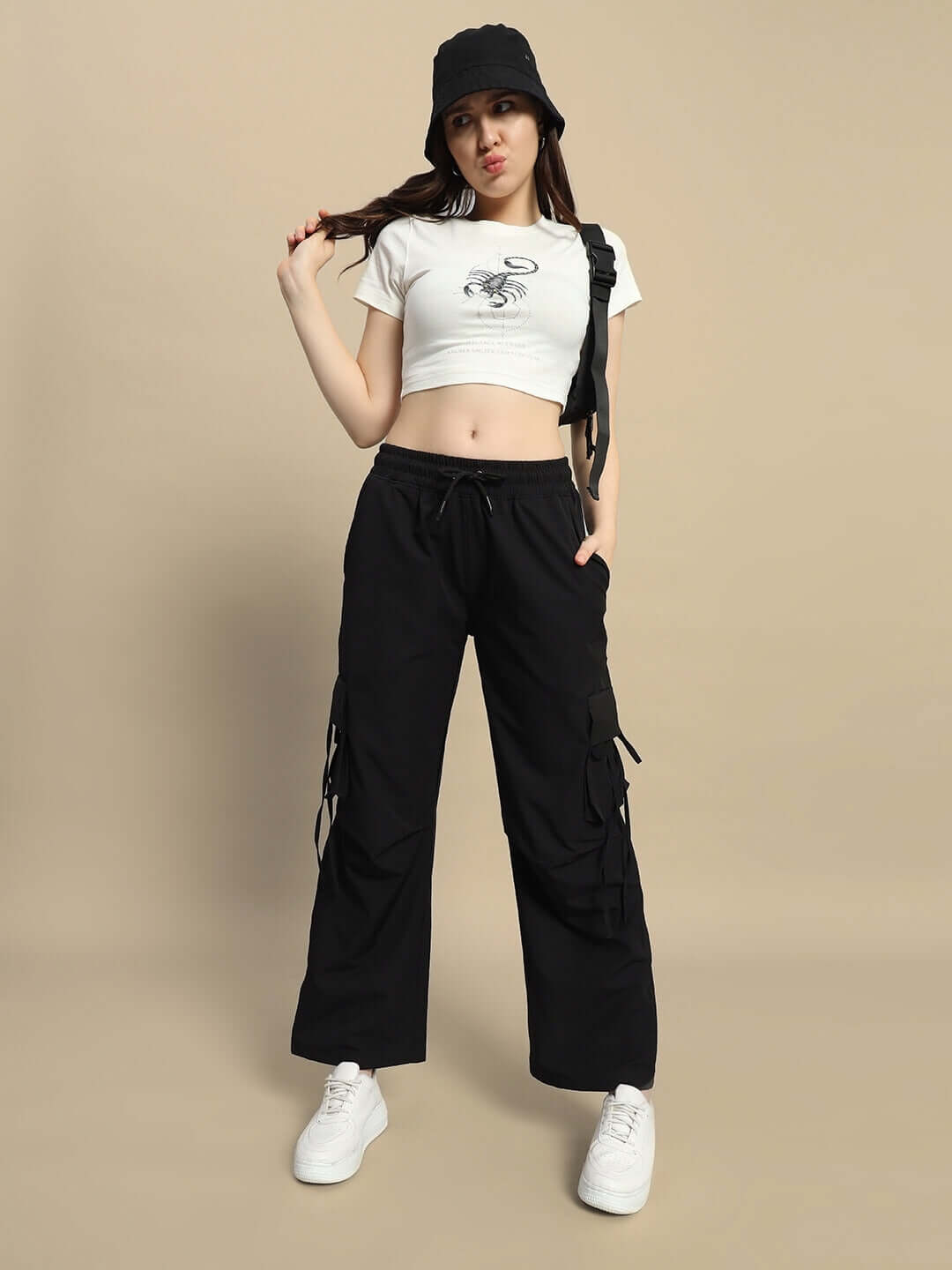 Model wearing women's black RAMROD parachute cargo pants with adjustable fit for customized sizing, styled with a white crop top and sneakers.