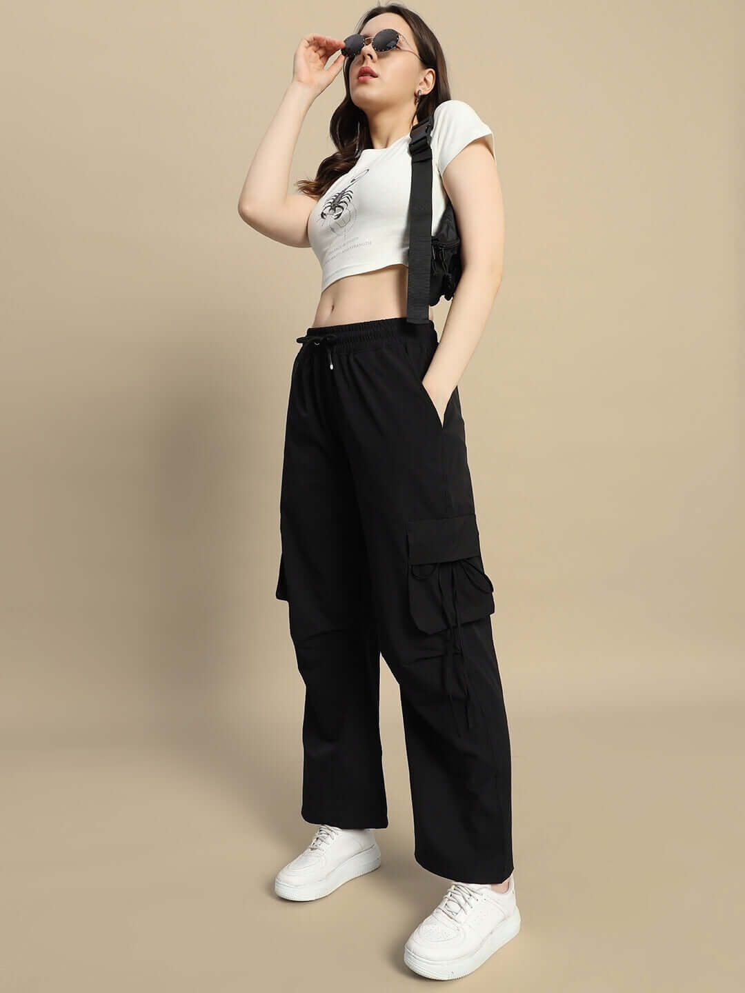 Women's black Ramrod parachute cargo pants with pockets, styled with a white crop top, sunglasses, and sneakers.