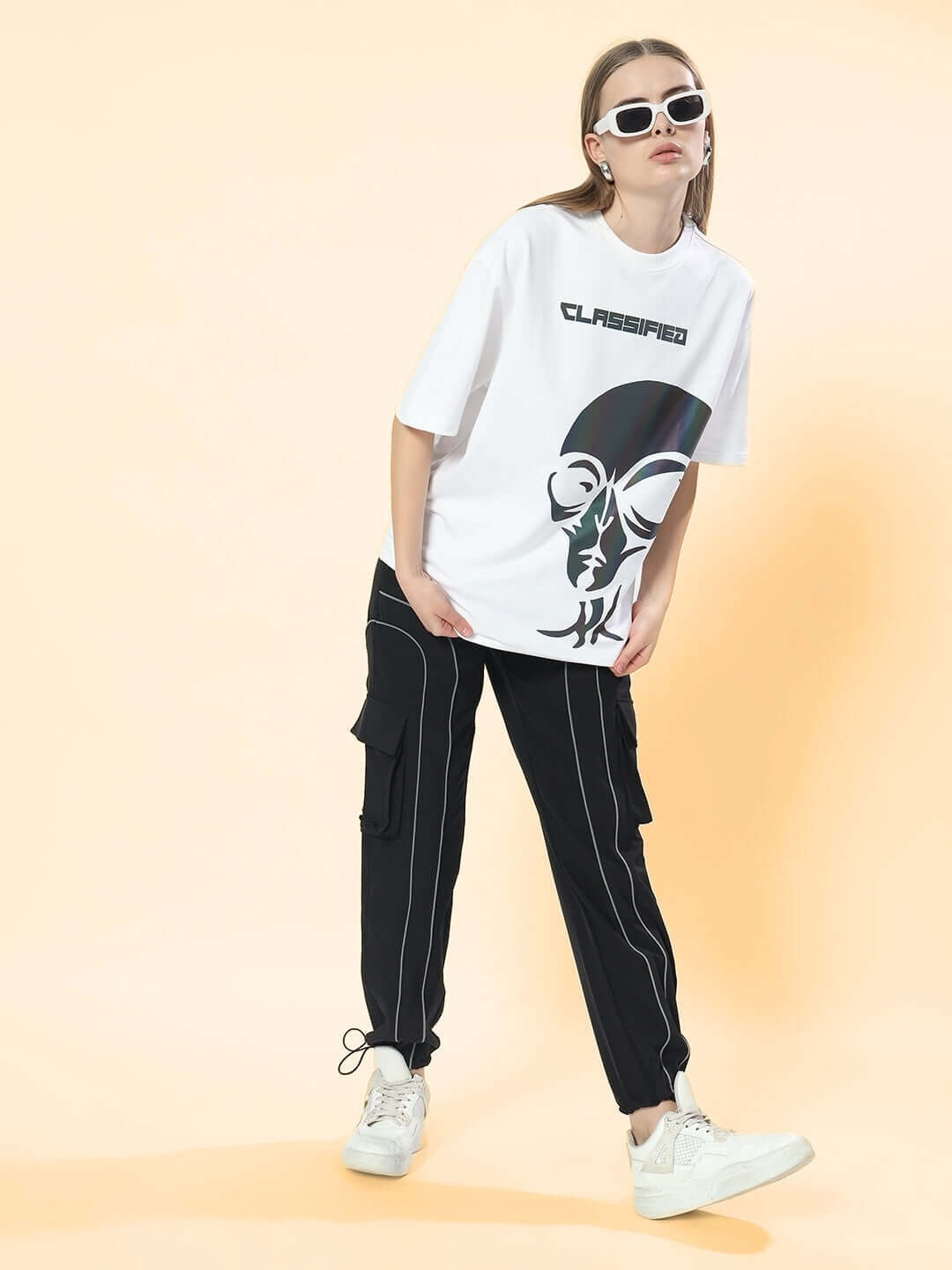 Woman wearing black women's ray reflector parachute cargo pants with a graphic t-shirt and white sneakers, standing against a soft gradient background.