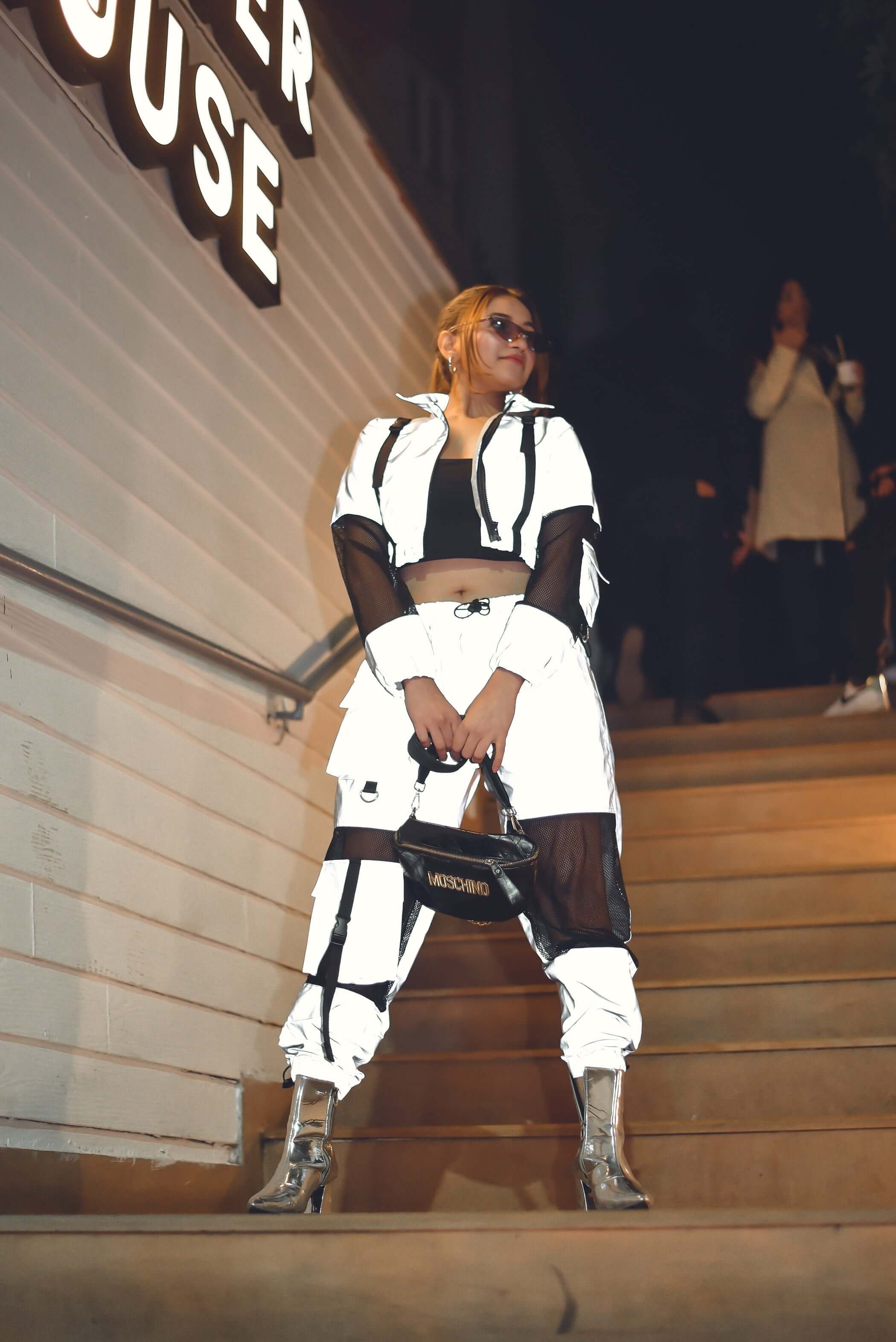 Model wearing WOMEN'S REFLECTOR CO-ORD SET CARGO PANTS WITH JACKET, standing on steps at night, showcasing edgy street style fashion.