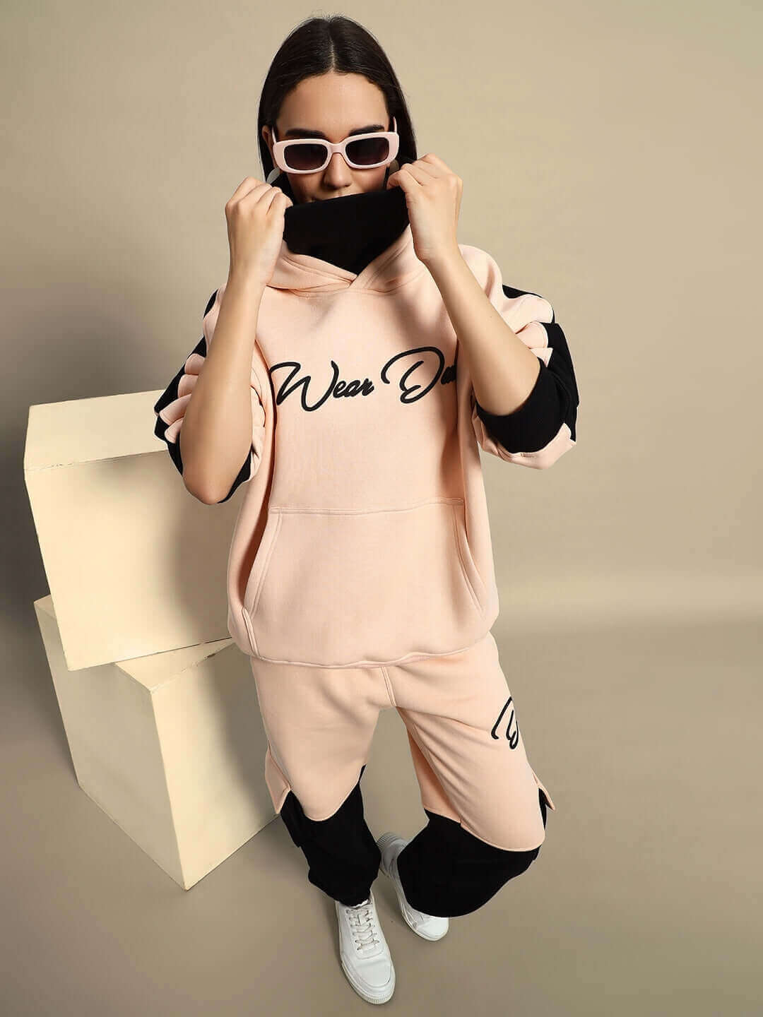 Woman modeling beige-black fleece hoodie with sunglasses, showcasing stylish women's regiment fashion look.