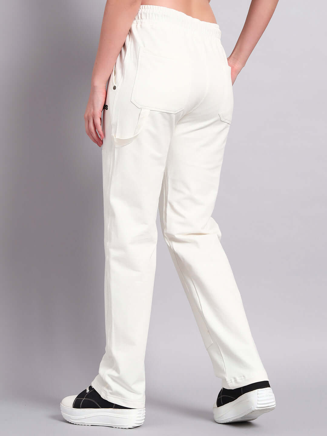 Model wearing women's white Regulus relaxed-fit joggers by DUDS, showcasing back view with casual sneakers.