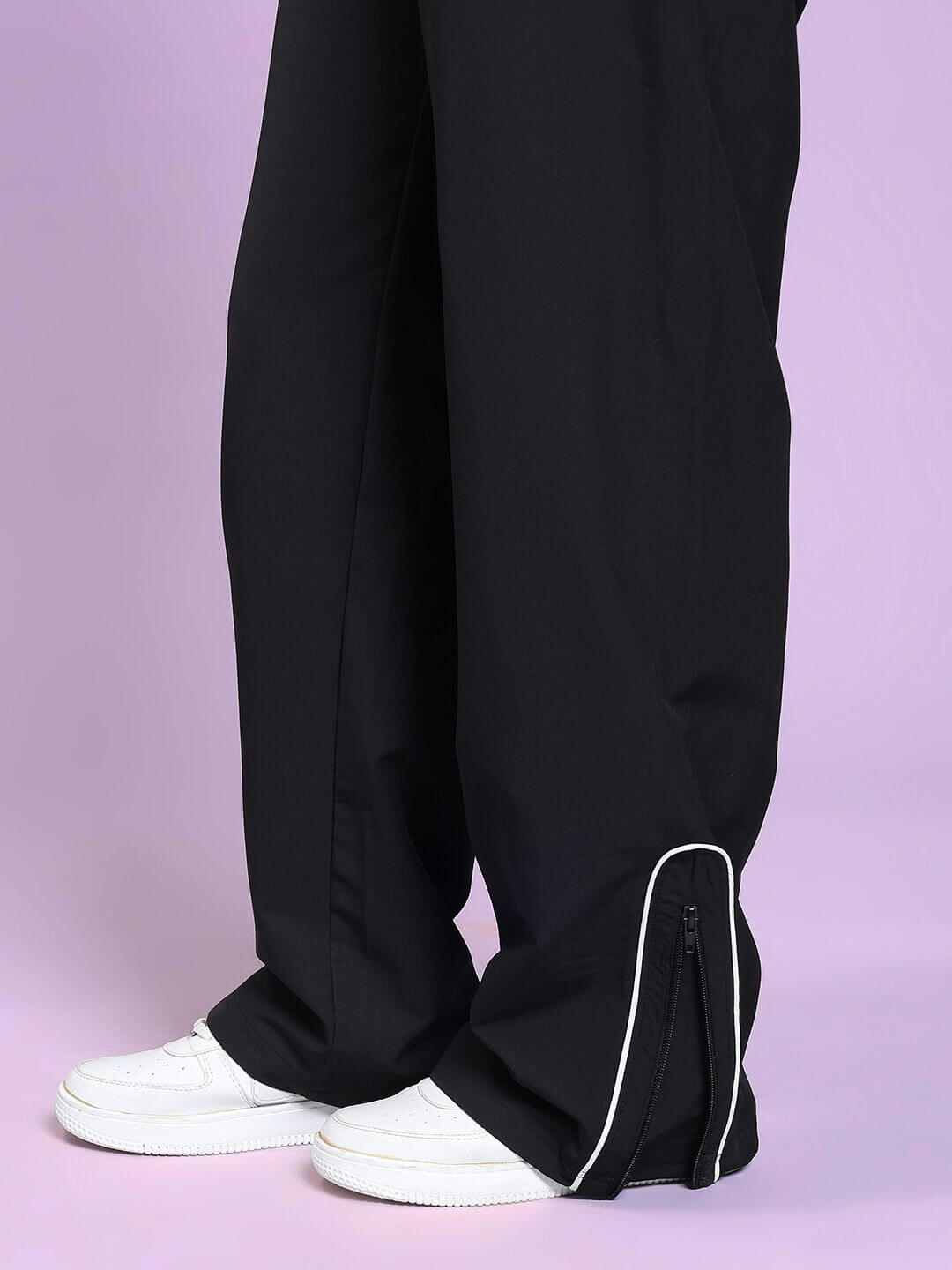 Close-up of WOMEN PERFACT RELAXED-FIT JOGGER BLACK paired with white shoes, highlighting zip detail and relaxed fit design on a pastel background.