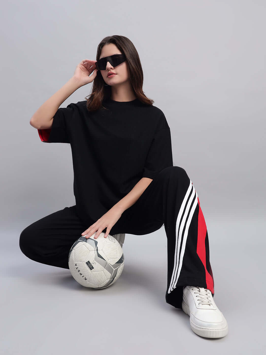 Model wearing Women's Tangle Relaxed-Fit Joggers in black-red, kneeling with a soccer ball, showcasing sporty and stylish pants.