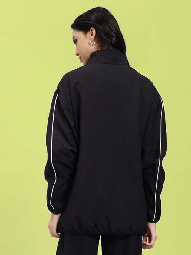 Back view of WOMEN RELIGHT RELAXED FIT JACKET BLACK with reflective trims on sleeves, emphasizing urban style and night visibility.
