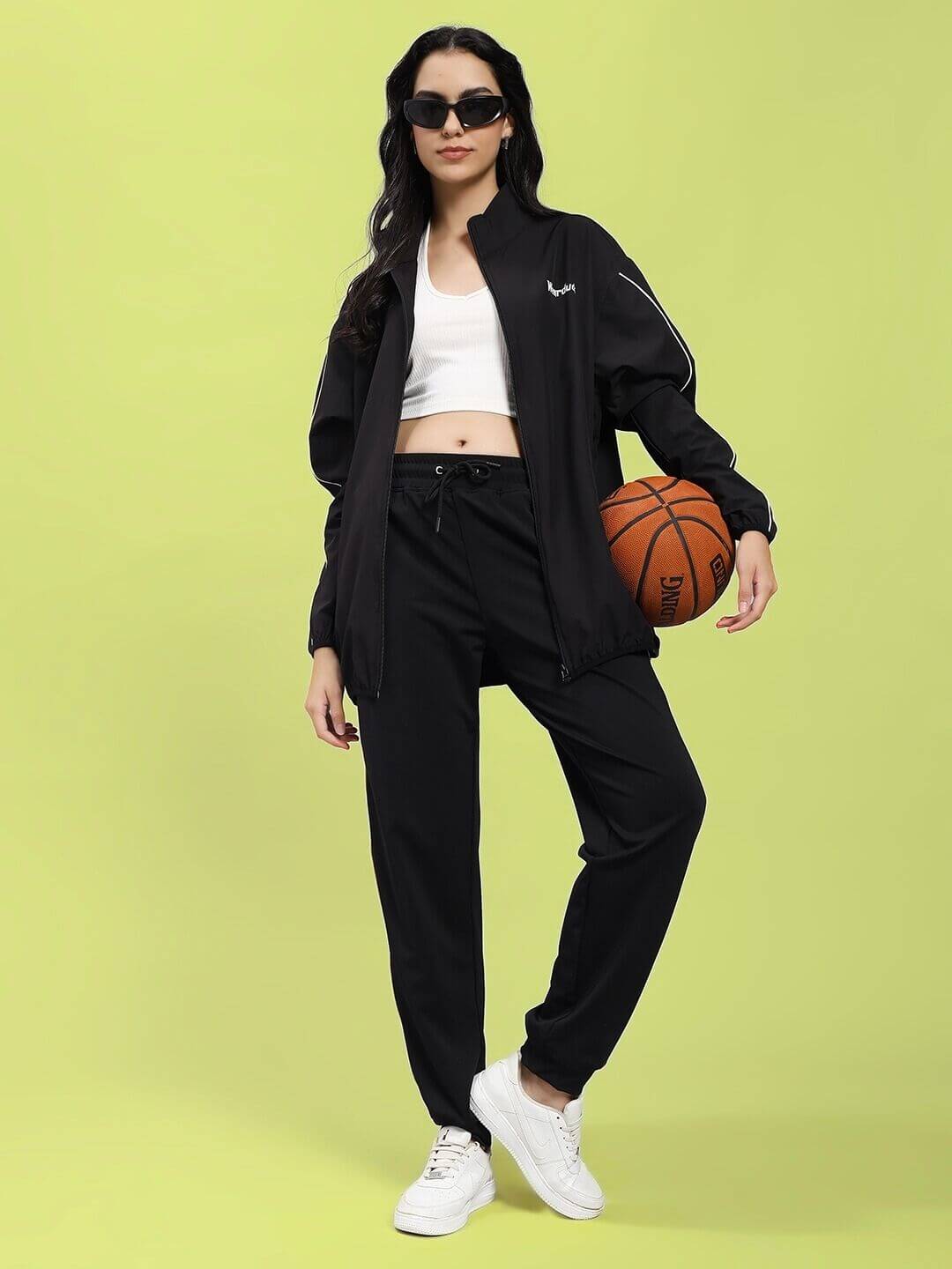 Woman wearing WOMEN RELIGHT RELAXED FIT JACKET BLACK with reflective trims, urban style, holding basketball.
