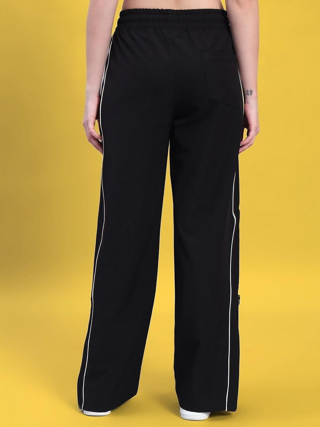 Back view of WOMEN'S RELIGHT Relaxed-Fit Joggers in black, showcasing custom fit design with stylish seams, set against a yellow background.