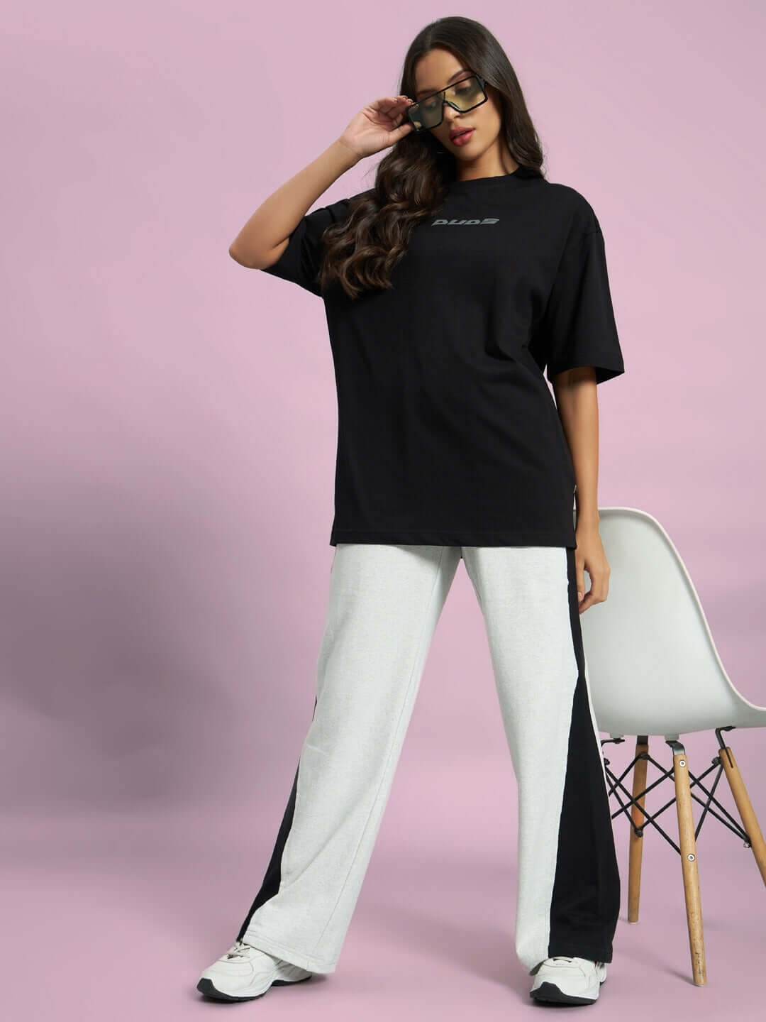 Woman wearing melange grey-black joggers with side contrast, standing in stylish pose, highlighting casual sporty outfit against pink backdrop.