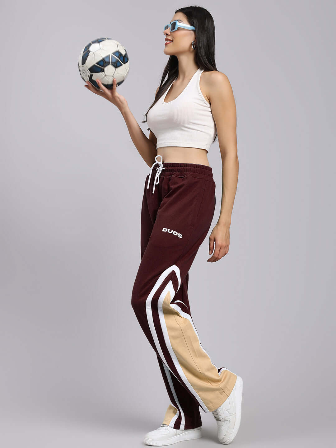 Woman wearing maroon women's Rio One relaxed fit joggers by DUDS, holding a soccer ball, showcasing sporty and casual style.