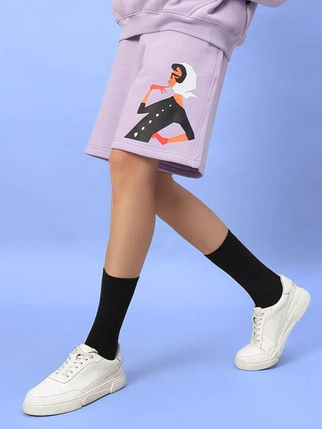 Alt Tag: WOMEN RITZY FLEECE SHORTS LILAC with graphic design, paired with sneakers and black socks, showcasing fashion style.