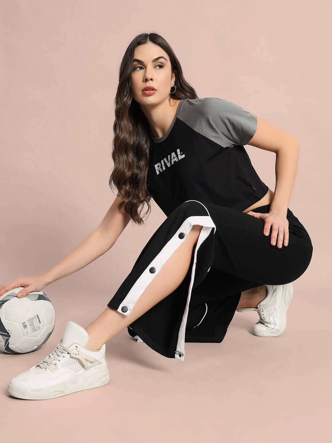 Woman wearing a black and grey crop-top and pants with a sports theme, featuring the word 'Rival' on the shirt, holding a soccer ball.