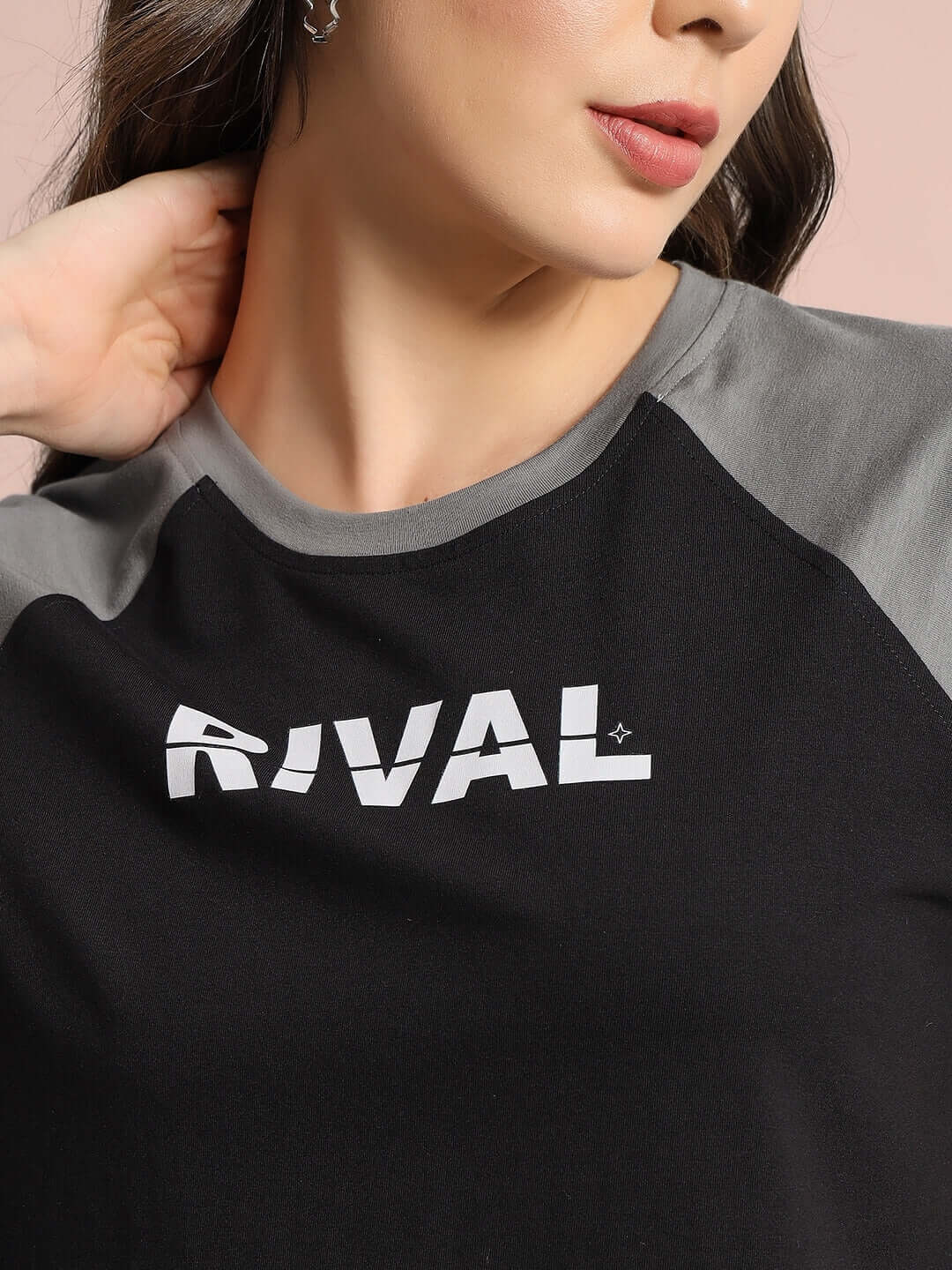 Close-up of a woman wearing a black and grey Women's Rival Raglan Crop-Top featuring "RIVAL" text on the chest.