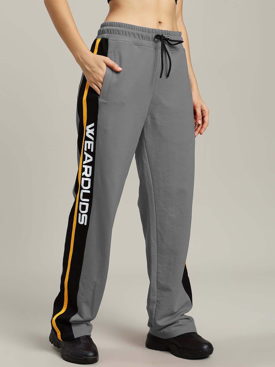 Woman wearing grey Women's Roger Relaxed-Fit Joggers with 'WEARDUDS' logo, side stripes, and black sneakers, showcasing casual style.