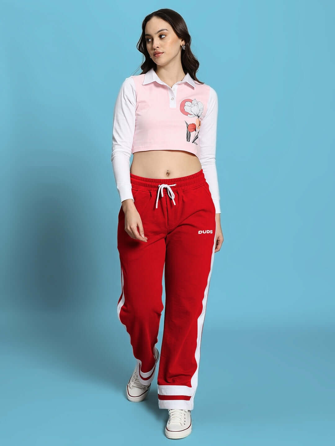 Woman wearing red Ronny side stripe joggers, styled with a white and pink top, set against a blue background.