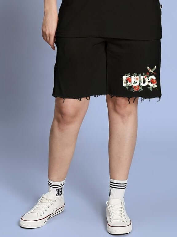 Woman wearing WOMEN ROSE CHARM RELAXED FIT SHORTS BLACK paired with white sneakers and socks, showcasing a casual and elegant style.