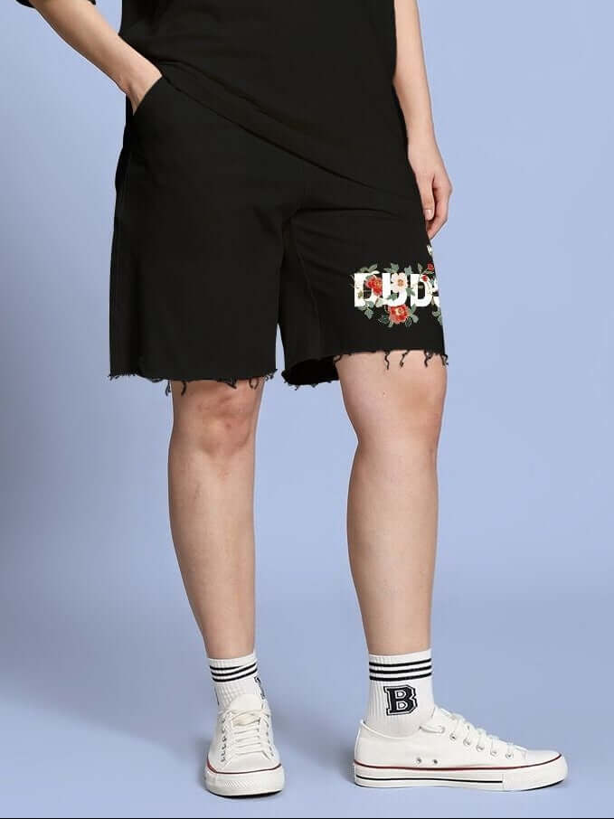 Woman wearing WOMEN ROSE CHARM RELAXED FIT SHORTS BLACK with floral patch, casual chic outfit.