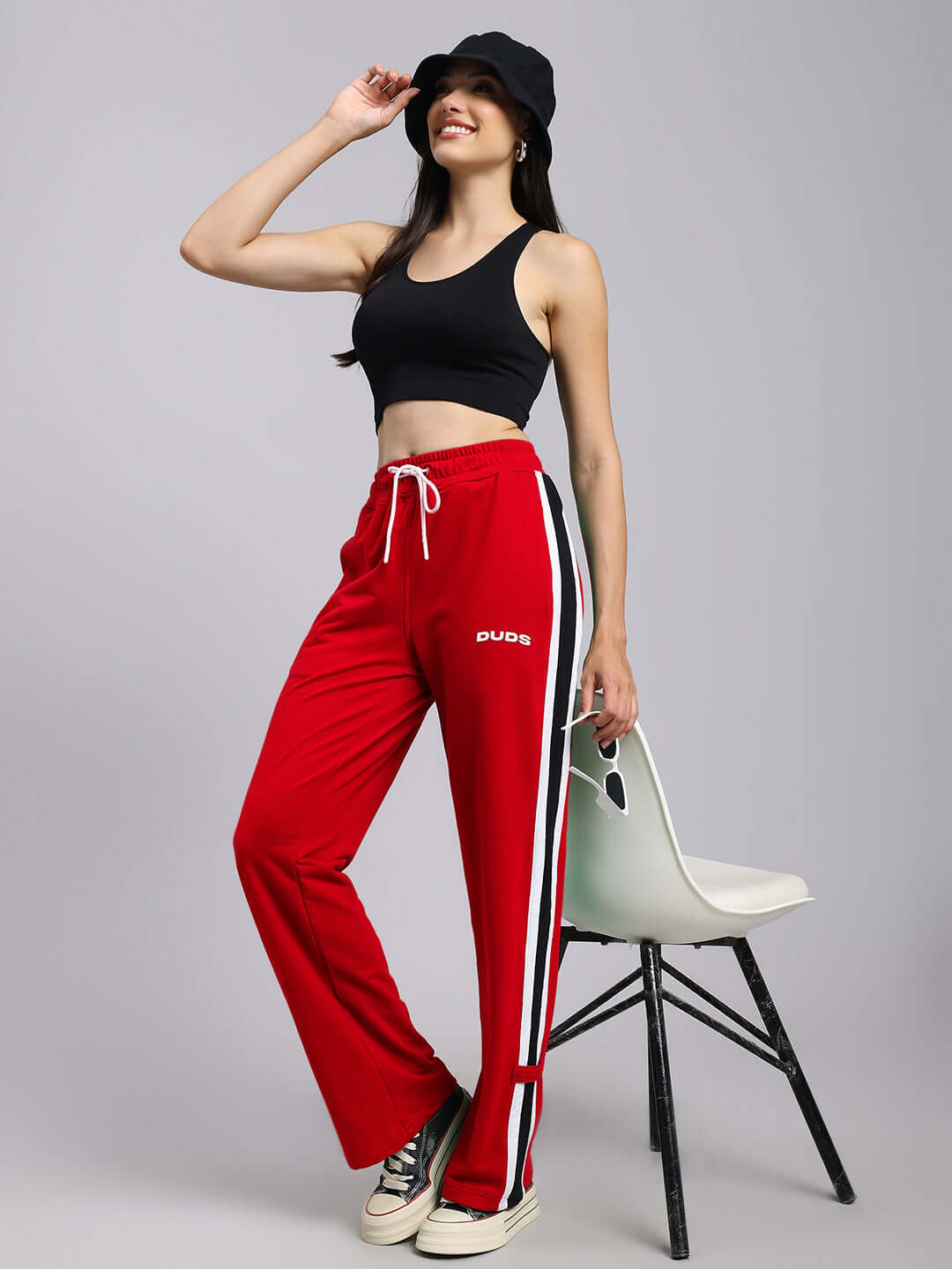 Woman wearing red Women's Rosston Relaxed Fit Joggers by DUDS, styled with a black crop top and sneakers, posing with a smile.