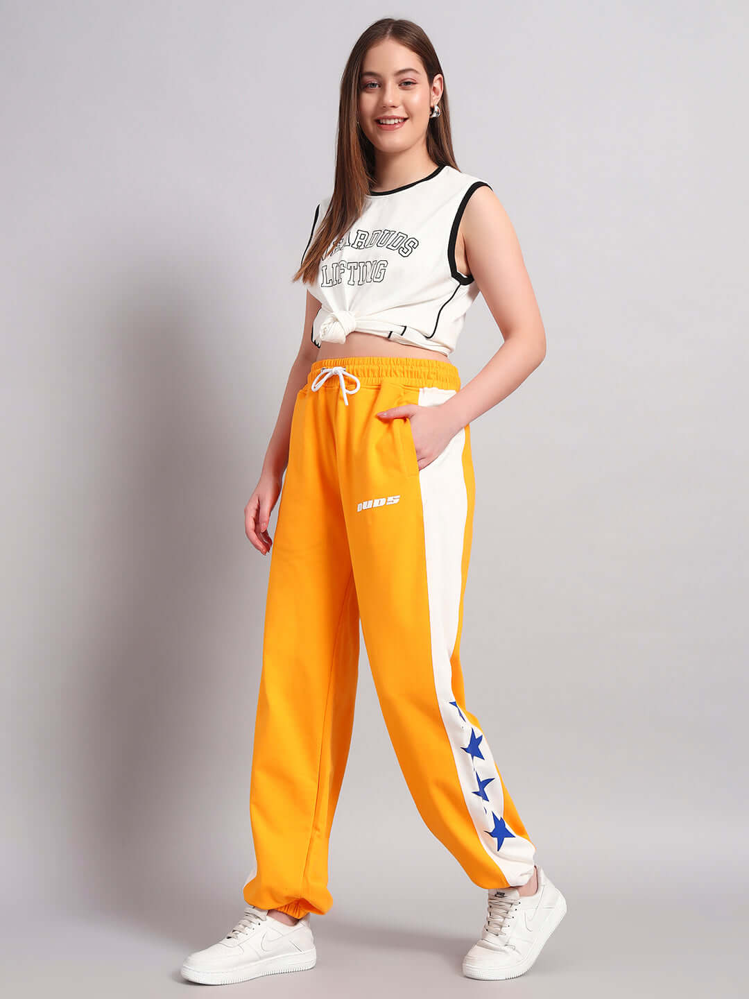 Woman wearing orange-white relaxed fit joggers with DUDS logo, paired with white sneakers, featuring side star design. Casual look for women.