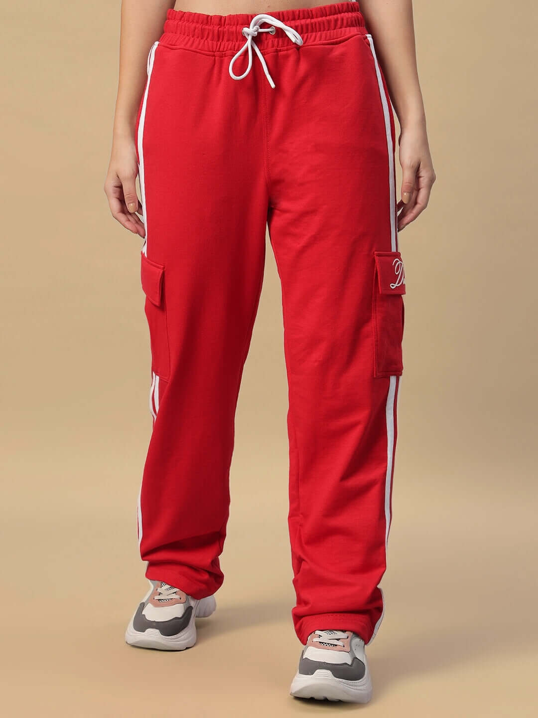 Women's Scotia Stripe Joggers in red with white stripes, featuring cargo pockets, displayed in a warm beige setting.