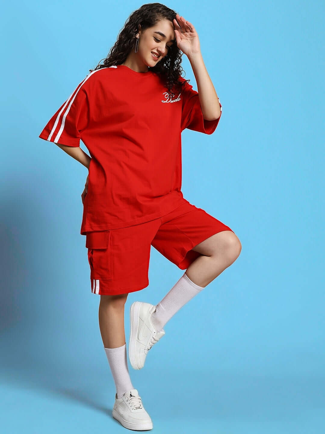 Woman wearing red WOMEN'S SCOTIA REGULAR FIT SHORTS with a matching top, posing stylishly against a blue background.