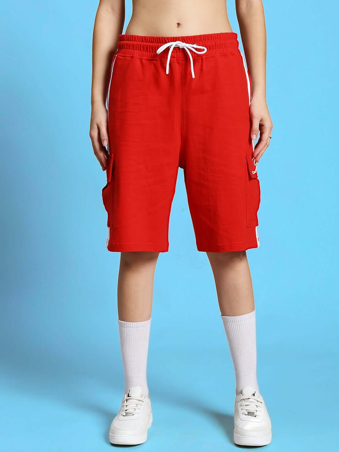 Model wearing WOMEN'S SCOTIA SUMMER CO-ORD SET RED, showcasing vibrant red shorts with white sneakers against a blue background.