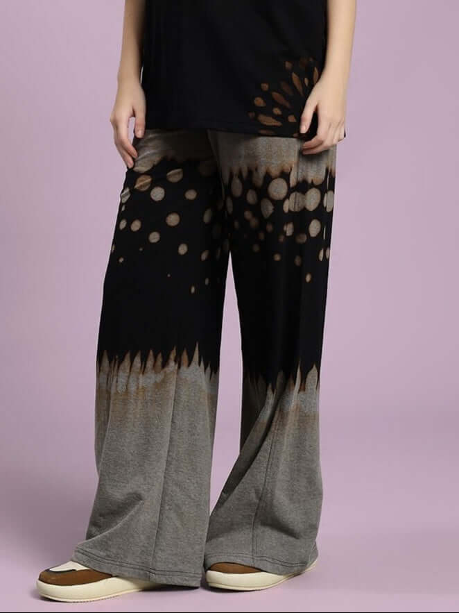 Person wearing WOMEN SHADOW SWIRL TIE-DYE JOGGER BLACK with artistic swirl pattern standing on purple background.