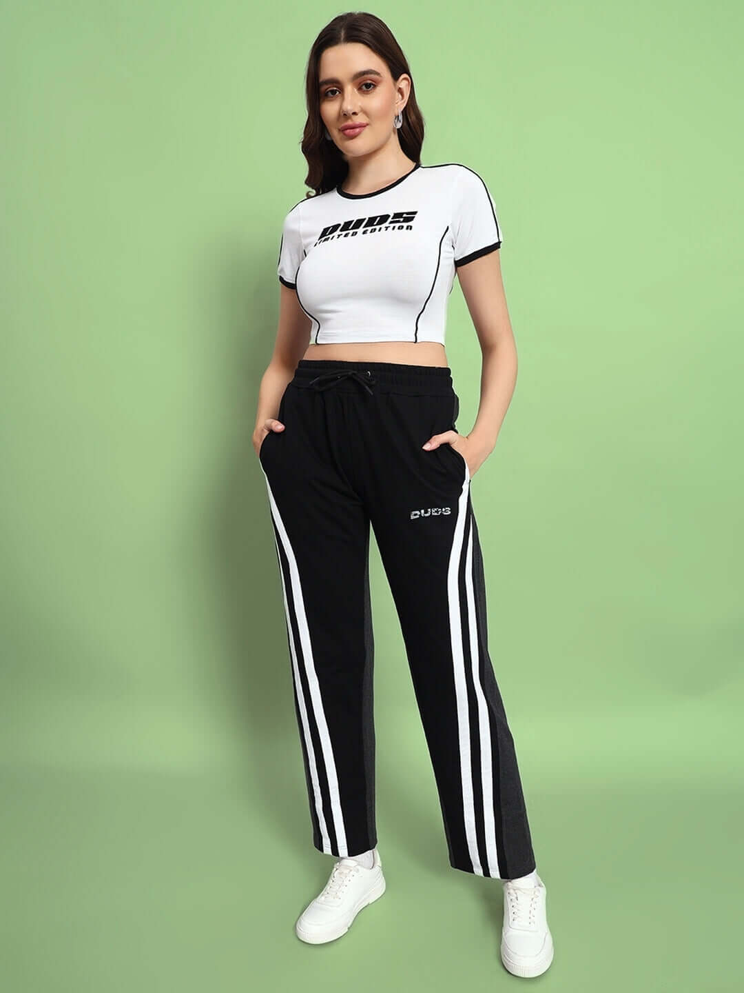 Woman wearing black grey Korean baggy joggers with white stripes, hands in pockets, paired with a white cropped top, posing confidently.