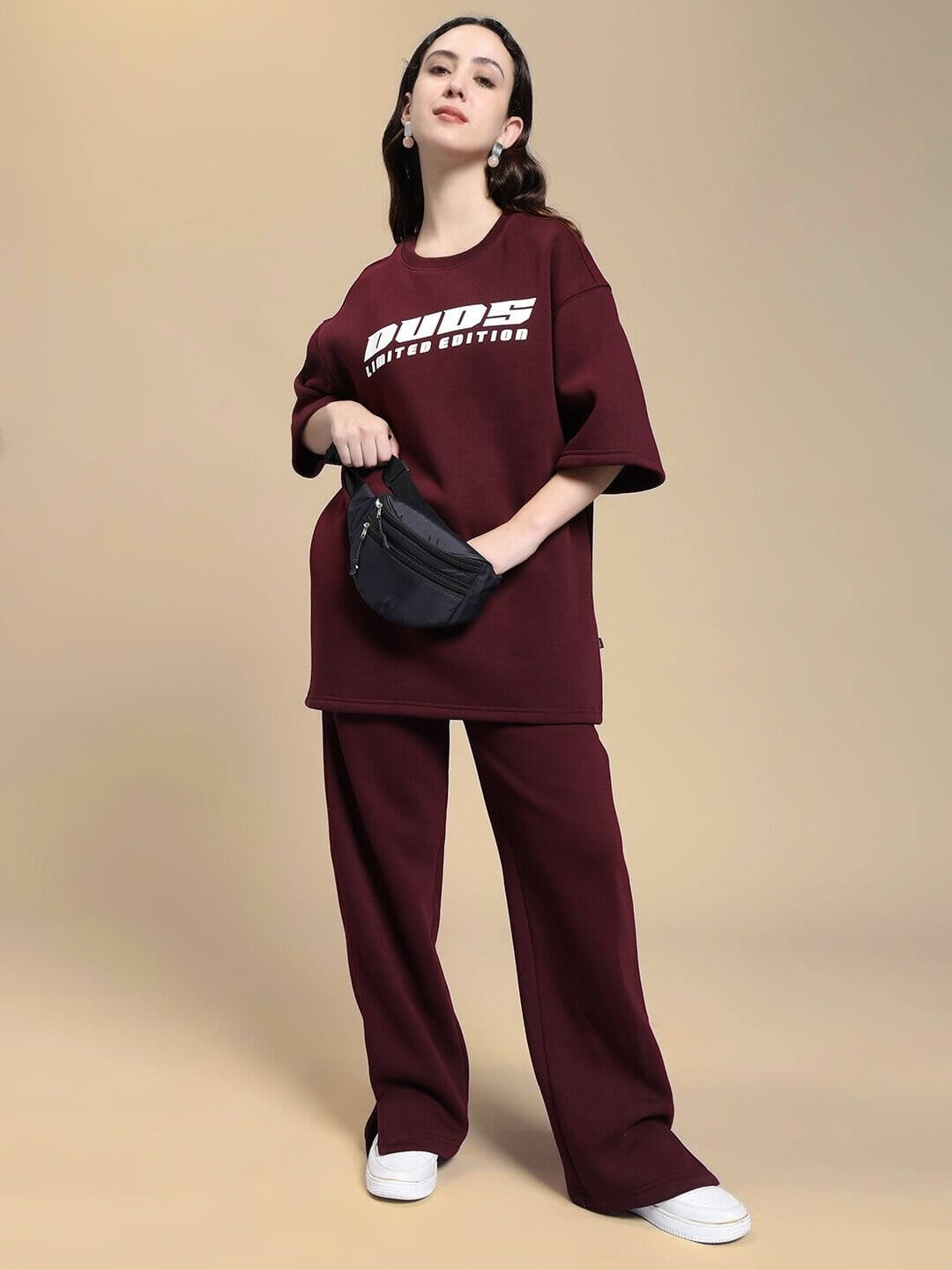 Woman wearing WOMEN SKODA FLEECE OVERSIZED T-SHIRT MAROON paired with matching pants, posing with a black crossbody bag and white sneakers
