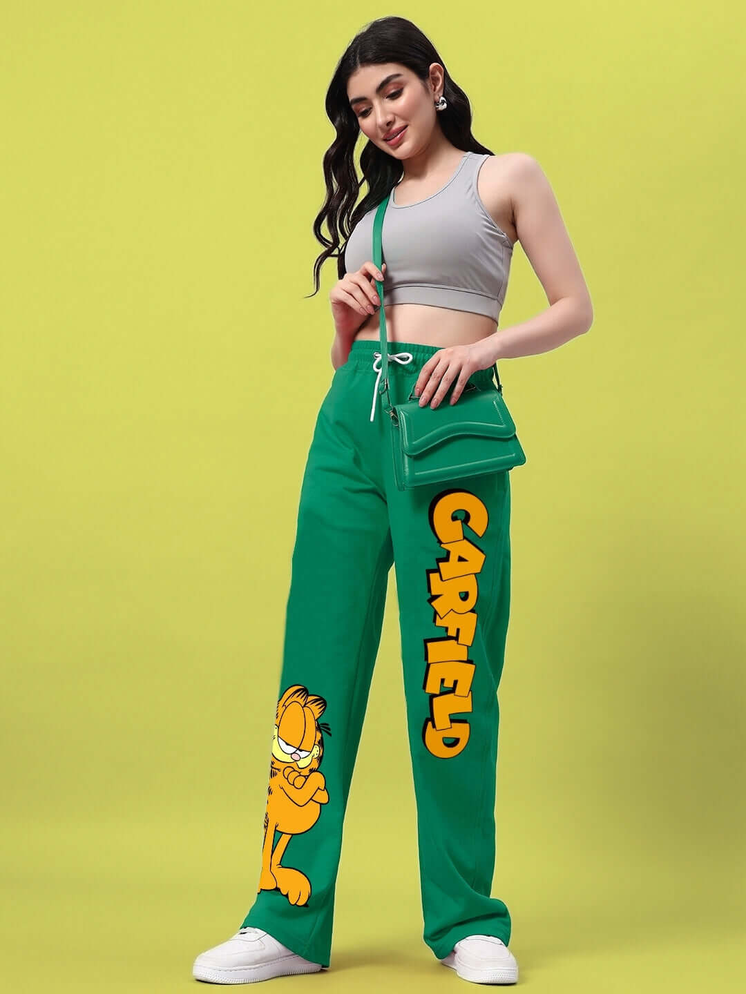 Woman wearing WOMEN'S SMUG GARFIELD RELAXED FIT JOGGER GREEN with cartoon prints, standing against a yellow background.